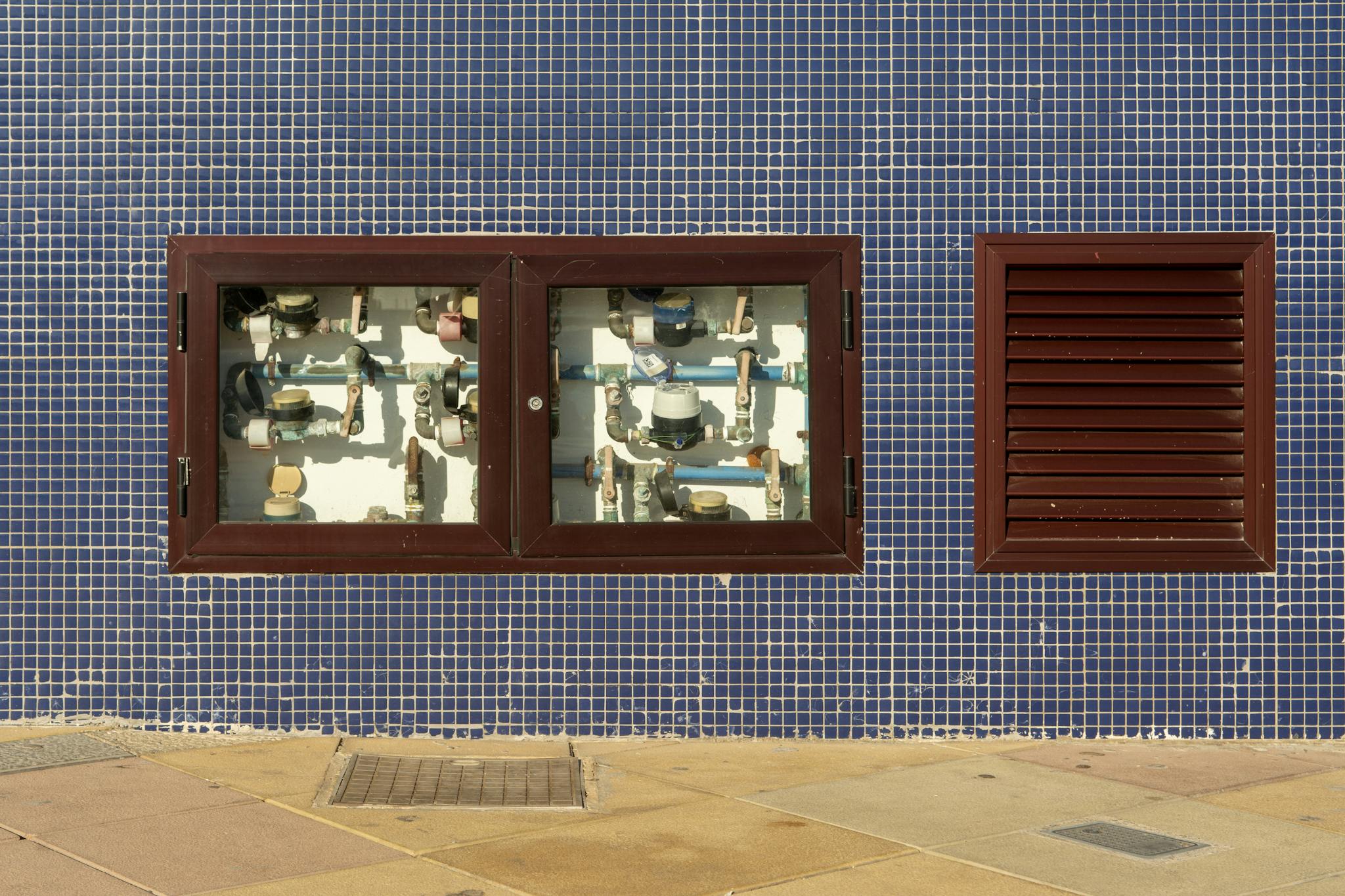 Close-up of a tiled wall with exposed water meters and vent in Arinaga, Spain.